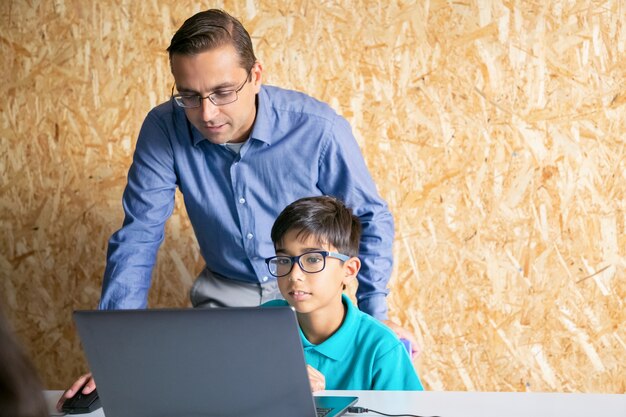 Profesor de contenido de mediana edad ayudando al niño con la lección y explicando el tema