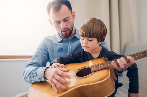 Foto gratuita profesor dando clases de guitarra en casa al niño
