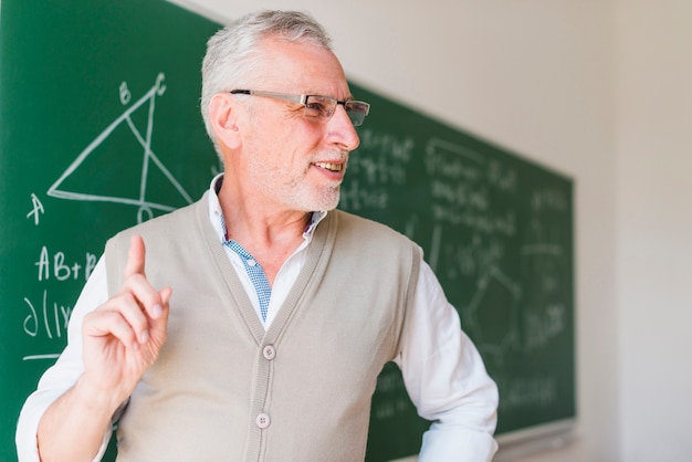 Profesor envejecido que da una conferencia cerca de la pizarra en sala de clase