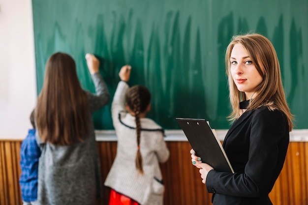 Profesor de la escuela con portapapeles sobre fondo de pizarra y estudiantes