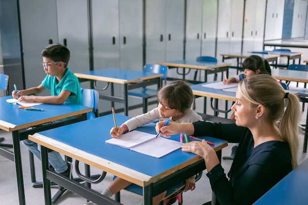 Profesor de escuela serio que ayuda a los alumnos a hacer frente a su tarea en clase