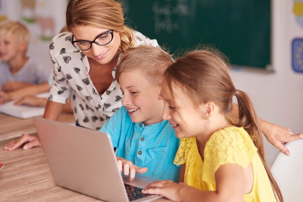 Profesor con estudiantes usando laptop en aula