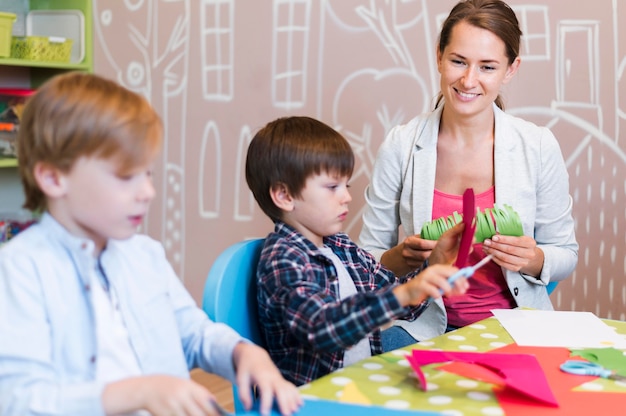 Foto gratuita profesor feliz cortando papel con niños