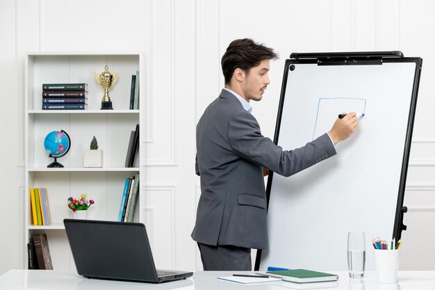 Profesor instructor inteligente en traje gris en el aula con computadora y tablero de dibujo de pizarra
