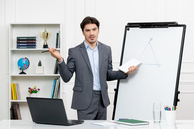 Profesor joven instructor en traje de oficina en la clase con computadora y pizarra explicando matemáticas