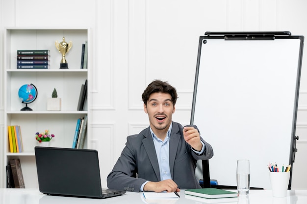 Profesor joven instructor en traje de oficina en la clase con computadora y pizarra sonriendo