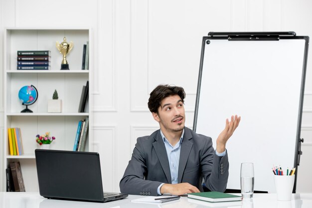 Profesor joven instructor en traje de oficina en la clase con computadora portátil y pizarra mirando hacia arriba