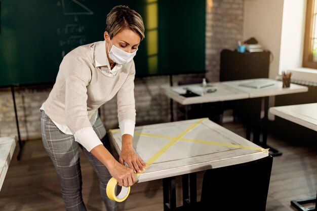 Foto gratuita profesor marcando mesas con cinta y preparando el aula para niños debido a la pandemia de coronavirus