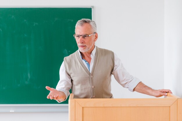 Profesor masculino mayor que explica la lección cerca de la pizarra