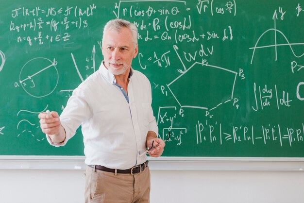 Profesor masculino sociable de pie en la pizarra y apuntando a mano