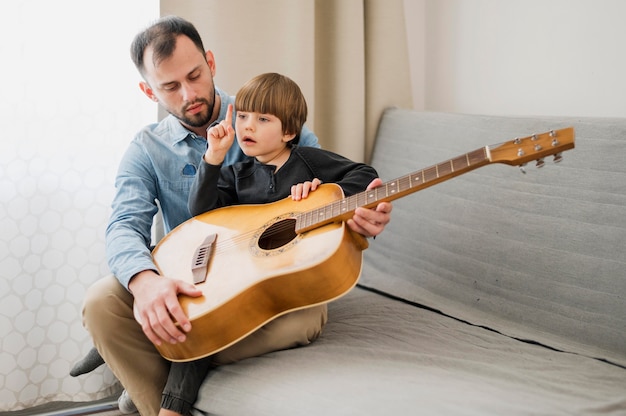 Profesor masculino tutoría a un niño en casa para clases de guitarra