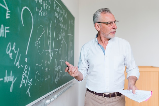 Profesor de matemáticas de edad avanzada que explica la fórmula en el aula