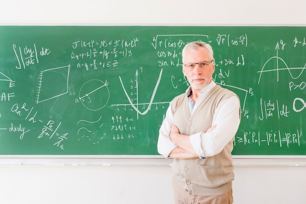 Profesor mayor de pie junto a la pizarra en el aula