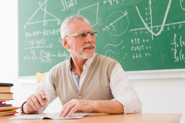 Profesor mayor que se sienta en el escritorio en sala de clase