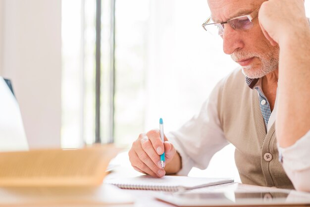 Profesor mayor en vidrios que escribe en el cuaderno en sala de clase