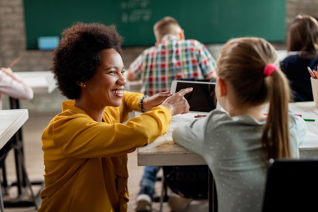 Profesor negro feliz y colegiala usando tableta digital en el aula