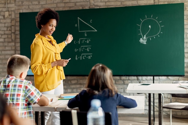 Profesor negro feliz enseñando matemáticas a estudiantes de primaria en el aula