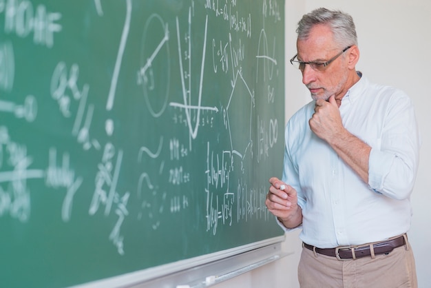 Profesor de sexo masculino pensativo que se coloca en la pizarra y que guarda tiza