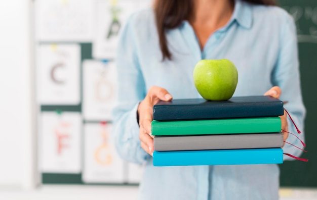 Profesor sonriente sosteniendo un montón de libros y una manzana