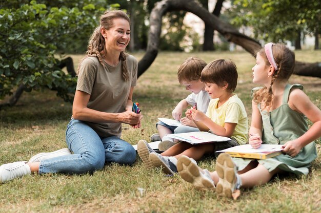 Profesor sonriente de tiro completo y niños al aire libre