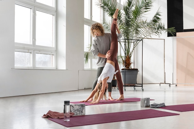 Profesor de yoga de tiro completo ayudando a mujer