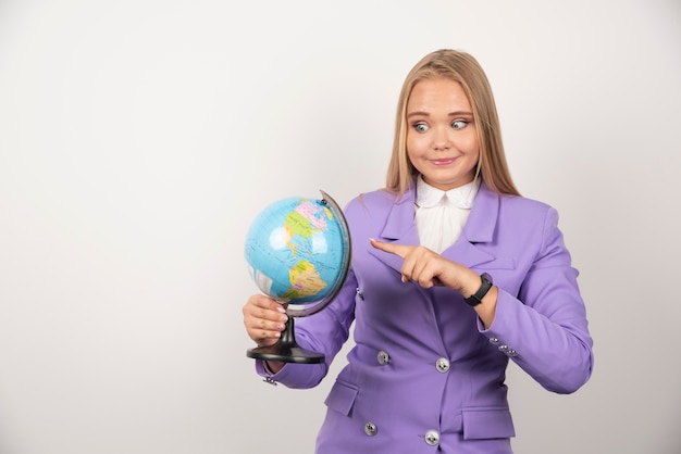 Profesora apuntando al globo en la pared blanca.