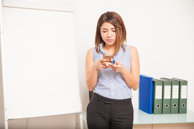 Foto gratuita profesora bastante joven que usa un teléfono inteligente y actualiza su estado en las redes sociales en el aula