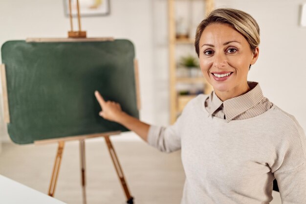 Profesora feliz señalando la pizarra mientras da clases en línea a sus alumnos