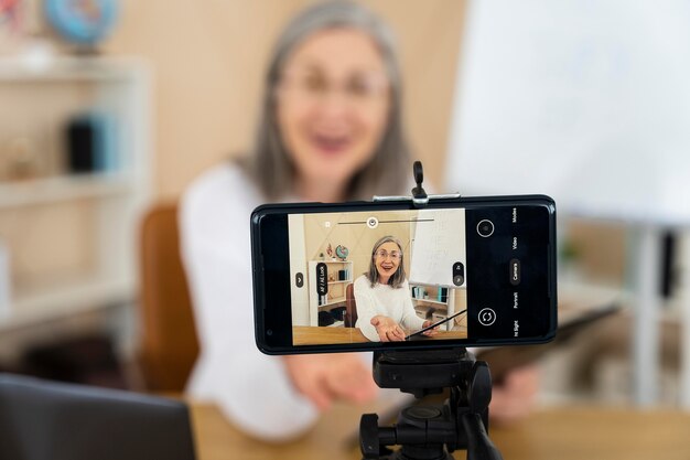 Profesora de inglés sonriente haciendo lecciones en línea en su teléfono inteligente