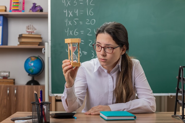 Profesora joven con gafas con reloj de arena mirándolo