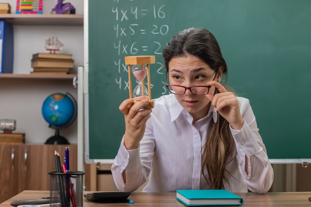 Profesora joven con gafas con reloj de arena mirándolo