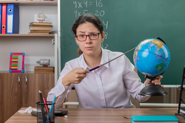 Profesora joven con gafas sosteniendo globo apuntando