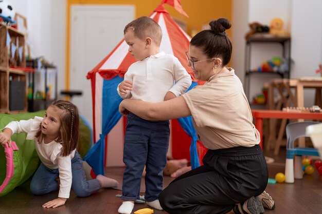 Profesora con niño y niña jugando en una carpa de circo sentada en el piso en el jardín de infantes