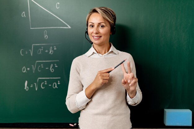 Profesora parada frente a la pizarra y explicando matemáticas durante la clase en línea.