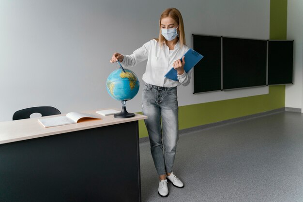 Foto gratuita profesora con portapapeles apuntando al mundo en el aula