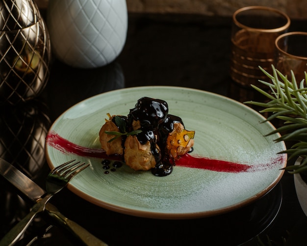 Profiteroles en salsa de chocolate dentro de un plato blanco.