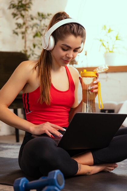 Programa deportivo en línea Mujer joven entrenando en casa con ayuda de videos de entrenamiento en línea