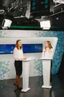 Foto gratuita programa de televisión con dos participantes en tribunes. mujeres emocionadas en el estudio de televisión, filmando un programa de televisión.