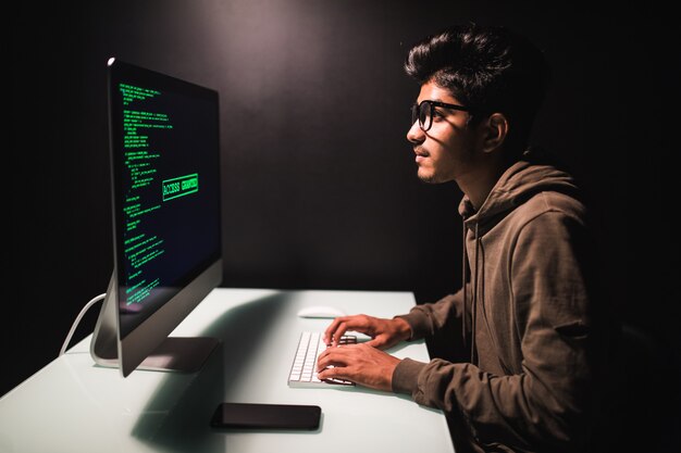 Programador indio masculino que trabaja en la computadora de escritorio en el escritorio blanco en oficina.