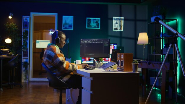 Programador negro trabajando remotamente en la oficina de casa escribiendo código en la computadora