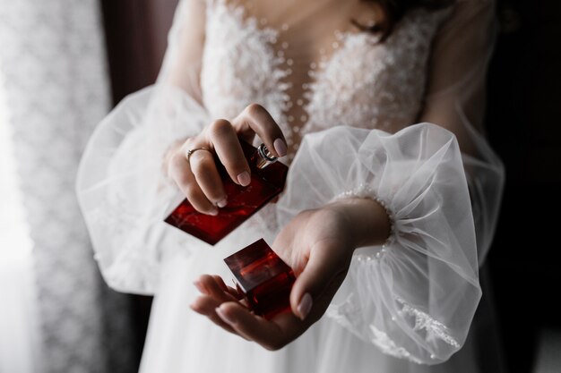 Prometida en vestido de moda blanco con hermosas mangas y perfume en manos