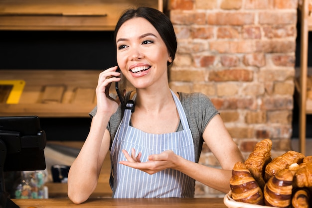 Propietario de panadería en el mostrador con croissant hablando por teléfono móvil