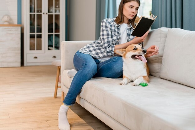 Foto gratuita propietario de perro y mujer leyendo un libro en el sofá