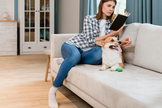 Propietario de perro y mujer leyendo un libro en el sofá