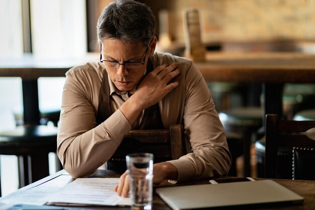 Propietario de pub adulto medio leyendo informes y revisando papeleo después de las horas de trabajo