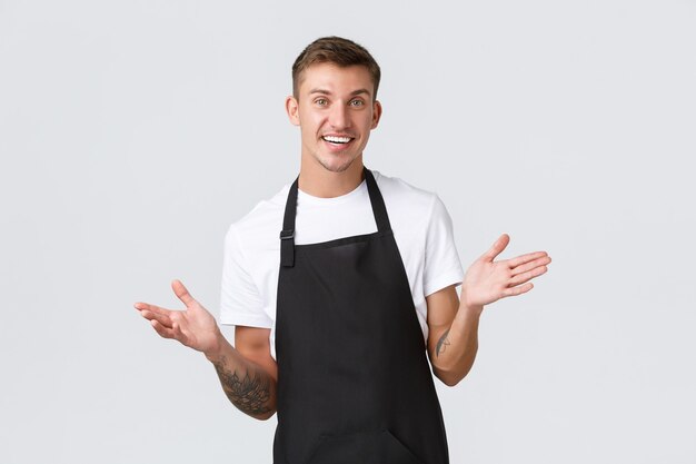 Propietarios de pequeñas empresas, cafetería y concepto de personal. Barista guapo de aspecto amistoso invitando a visitar el restaurante, estamos abiertos, sonriendo alegre como tomando el pedido de un huésped, fondo blanco.