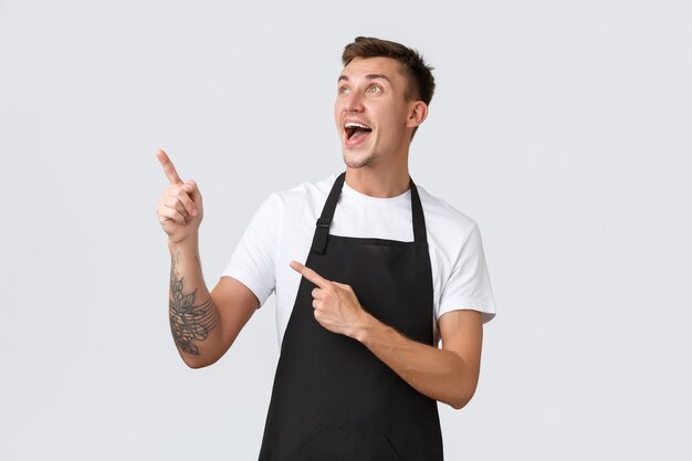 Propietarios de pequeñas empresas, cafetería y concepto de personal. Feliz sorprendido chico guapo sonriente trabajando en la cafetería, barista señalando con el dedo en la esquina superior izquierda, camarero regocijándose por las buenas noticias