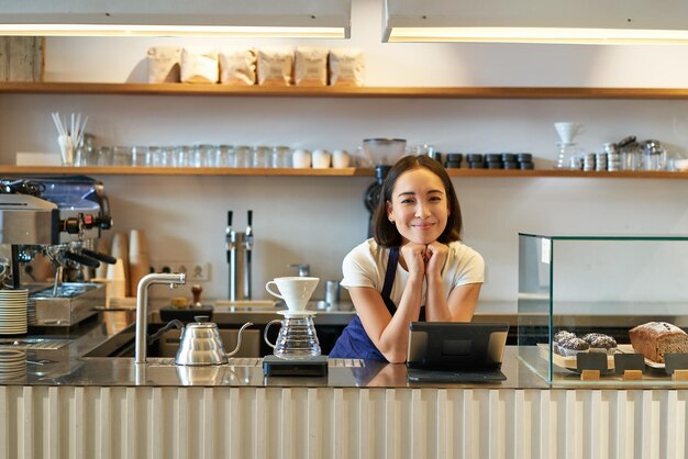 Propietarios de pequeñas empresas sonriente chica asiática barista de pie en el mostrador con kit de preparación de café de filtro