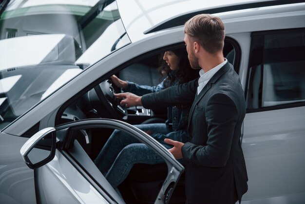 Prueba cómo se siente. Clienta y empresario barbudo con estilo moderno en el salón del automóvil