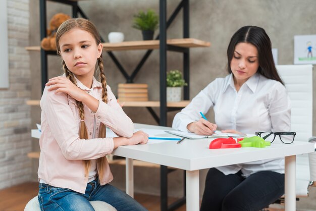 Psicólogo escribiendo notas en el portapapeles durante el encuentro con su niña deprimida